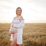 Femme enceinte blonde dans le champ de couronnes à des vêtements de sous-vêtements blancs au coucher du soleil.